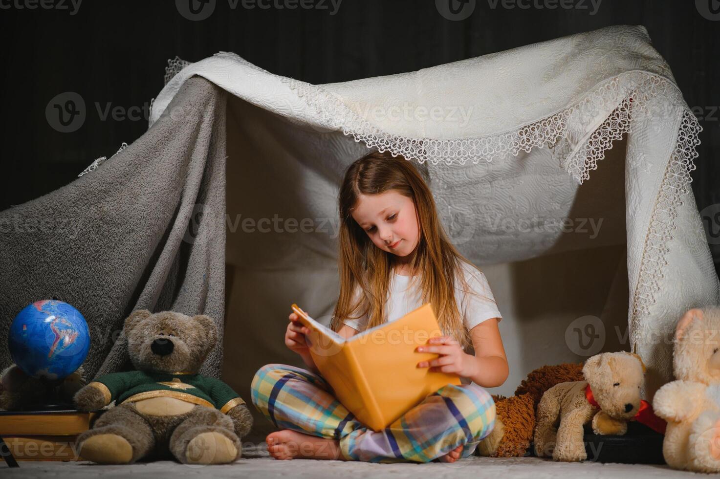 child girl reading with book and flashlight and teddy bear in tent. before going to bed photo