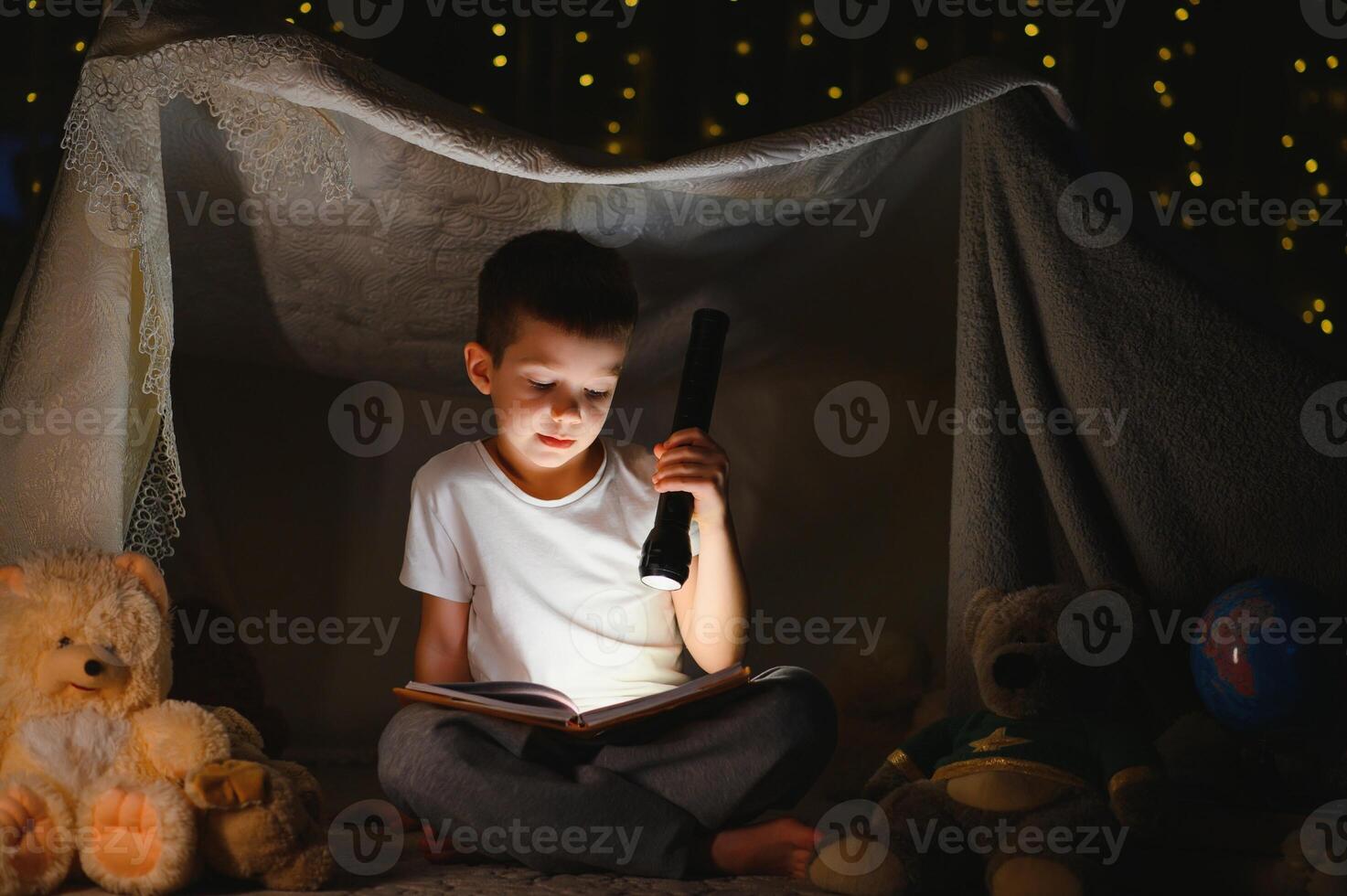 Preteen boy with flashlight reading book at home photo