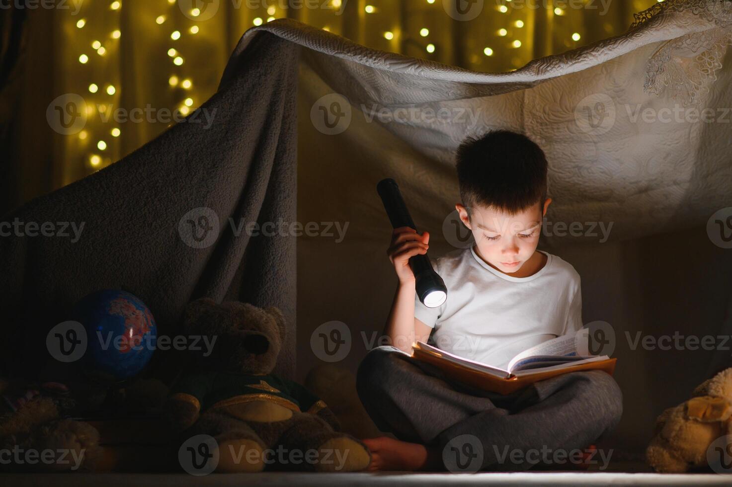 Preteen boy with flashlight reading book at home photo