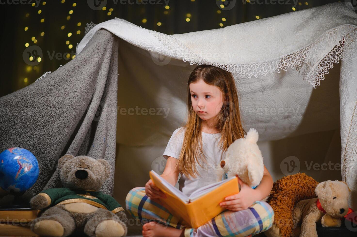 Little girl are reading a book with flashlights in tent. Happy girl playing at home. Funny lovely kid having fun in room. photo
