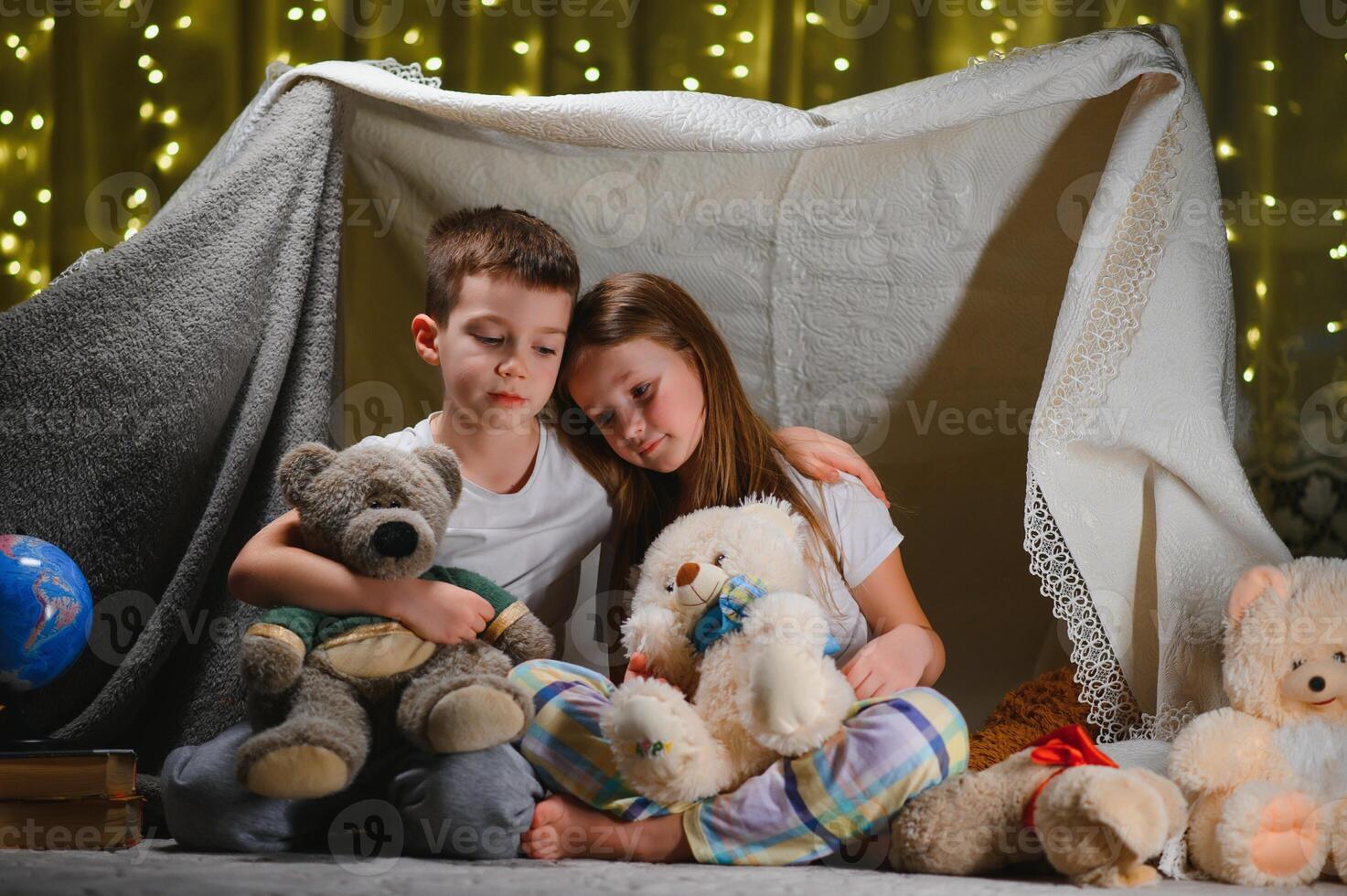 Two little child play at home in the evening to build a camping tent to read books with a flashlight and sleep inside. photo