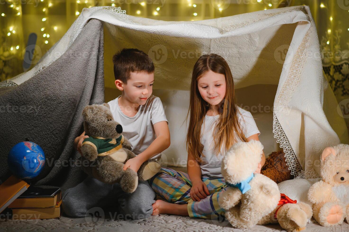 Two little child play at home in the evening to build a camping tent to read books with a flashlight and sleep inside. photo