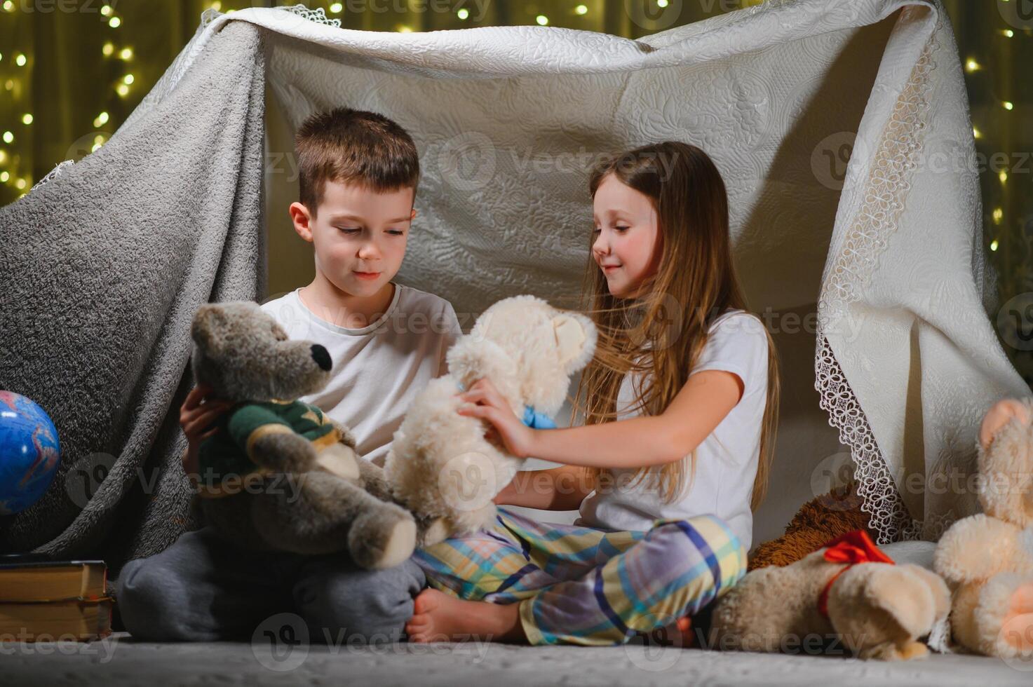 Two little children play at home in the evening to build a camping tent to read books with a flashlight and sleep inside photo