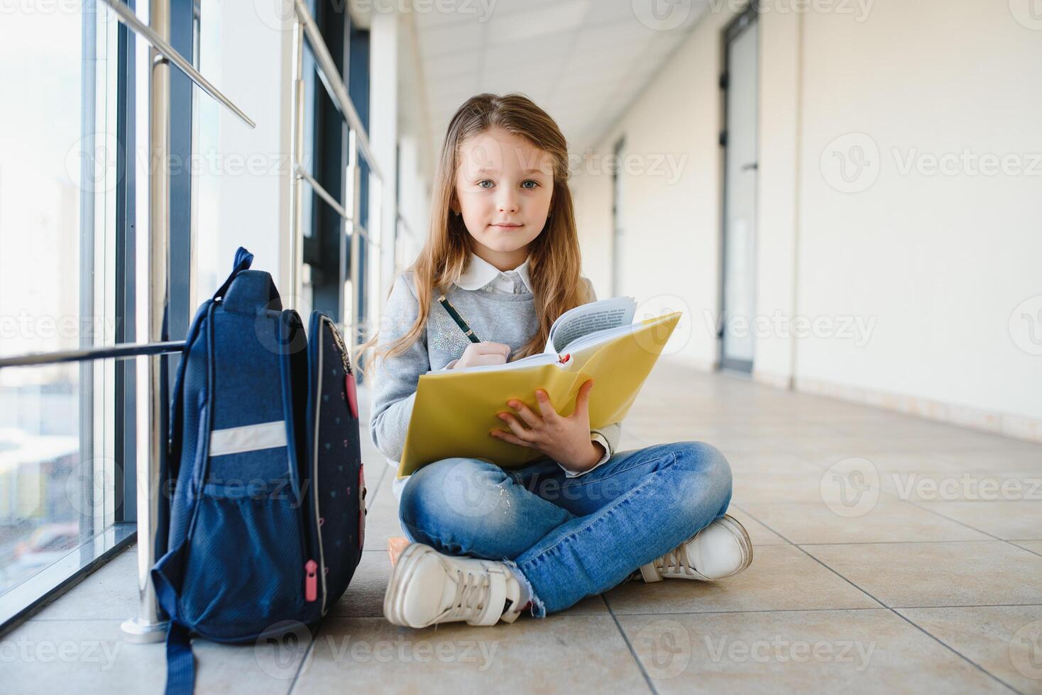 Front view of pretty blonde school girl holding many colorful notes and books. Clever teen girl smiling at camera, standing on corridor of international school photo