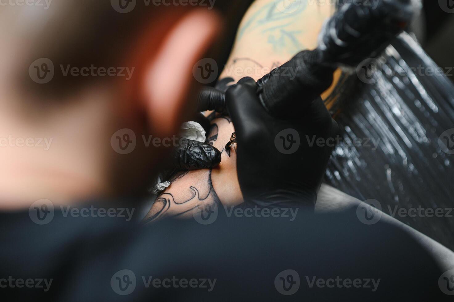 Cropped close up of a bearded tattoo artist working at his studio tattooing sleeve on the arm of his male client. Man getting tattooed by professional tattooist photo
