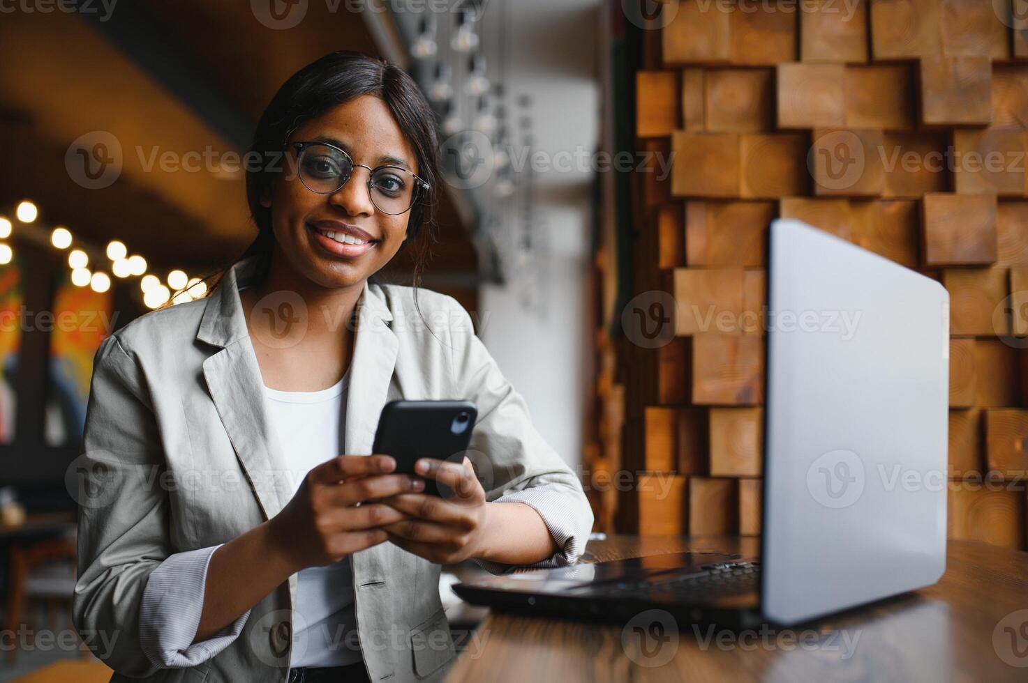 Young business woman is arranging the next business meeting in a modern coworking space by using a laptop. Young freelancer female is reading emails and other messages on a mobile phone. photo