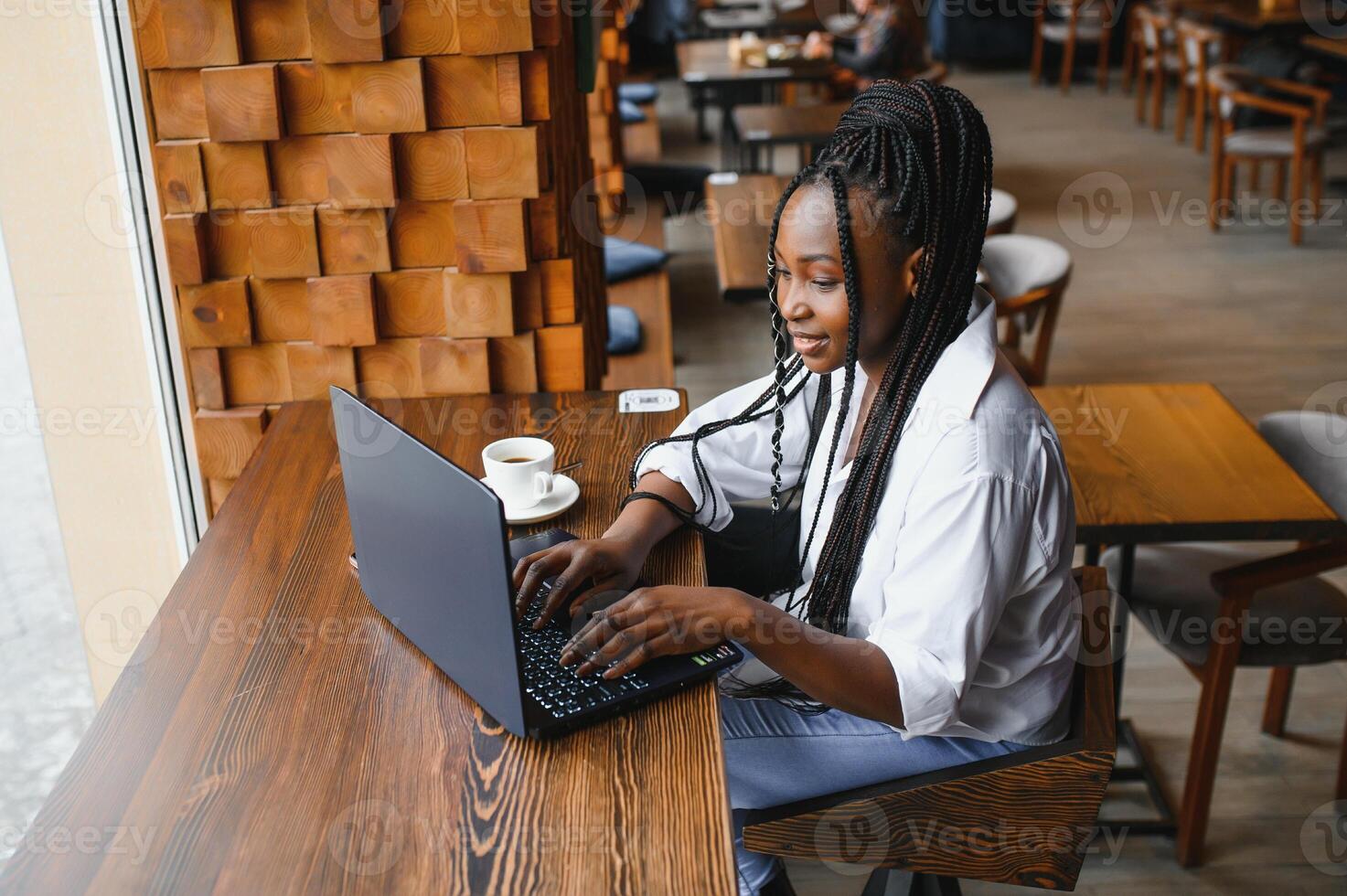 Beautiful african business woman waiting for the meeting in a co-working space and sitting with the portable computer. Hipster girl is surfing the web on a laptop during lunch. photo