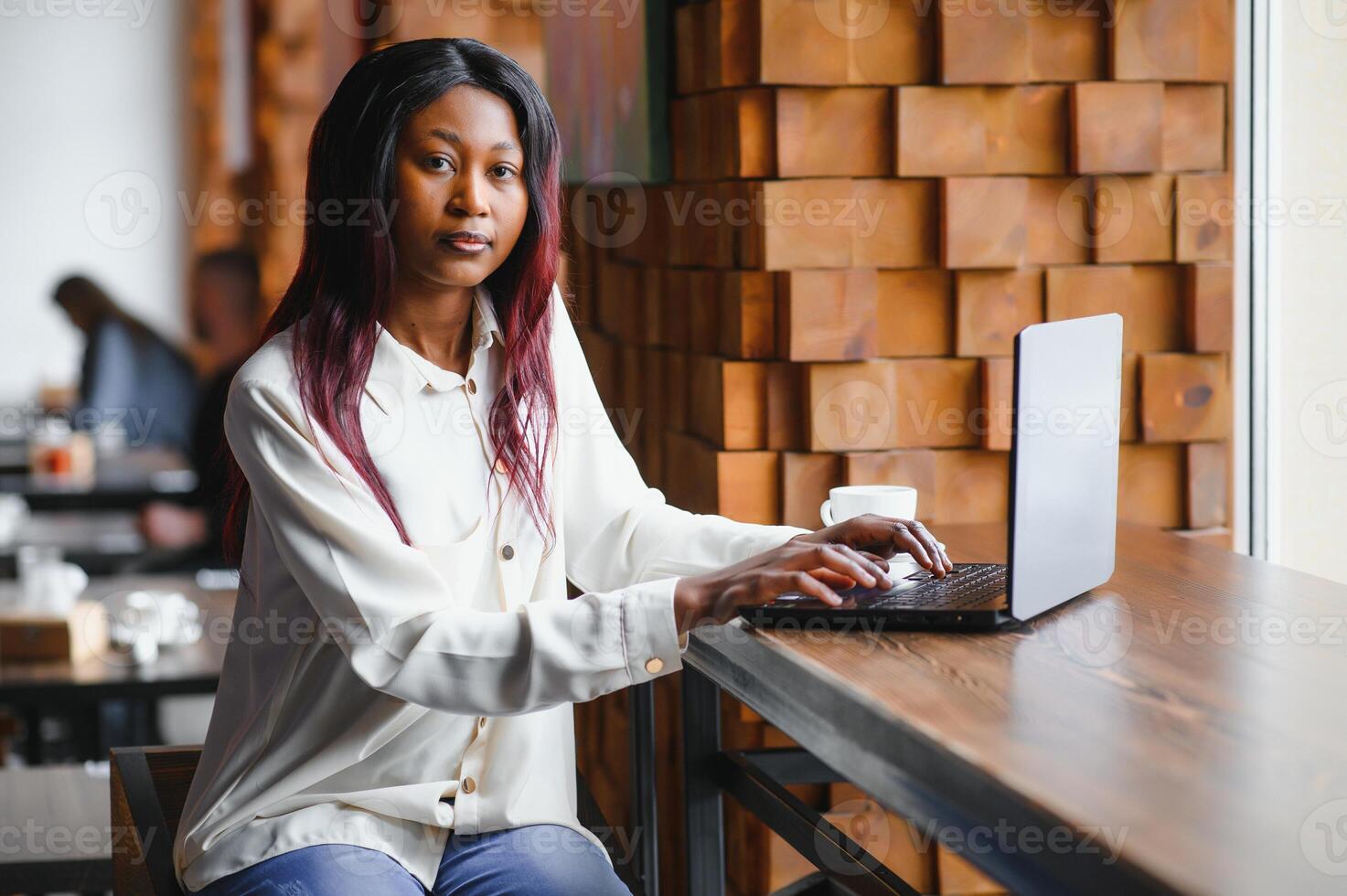 Beautiful african business woman waiting for the meeting in a co-working space and sitting with the portable computer. Hipster girl is surfing the web on a laptop during lunch. photo