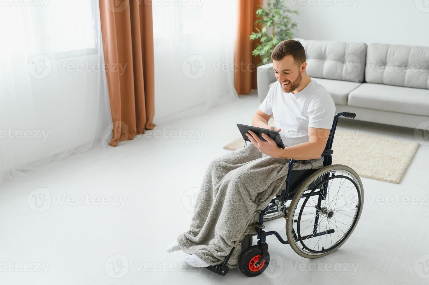 Man in wheelchair using tablet computer at home. Positive retired male with physical disability browsing web on touch pad, watching online indoors. photo