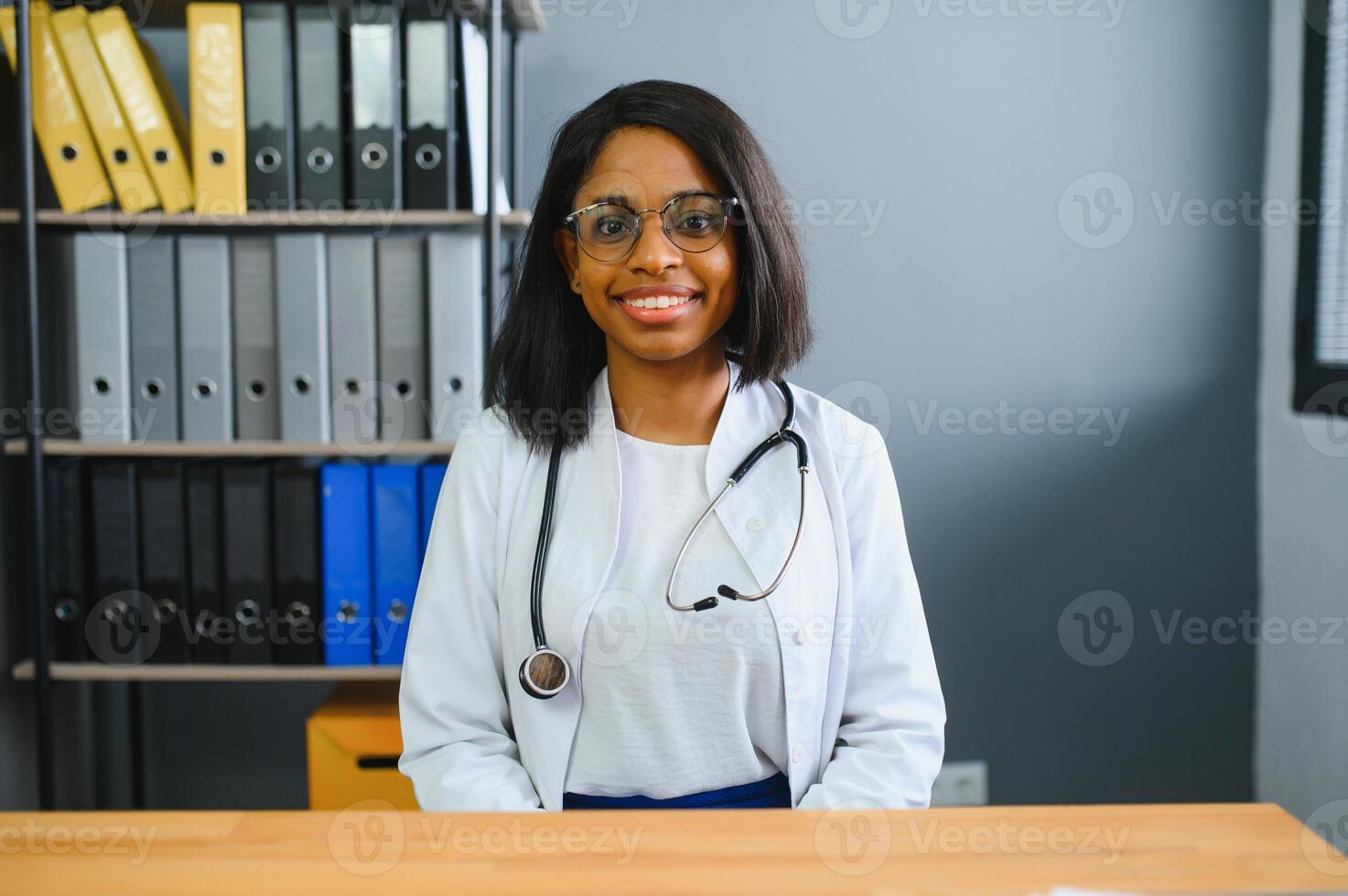 Smiling young adult indian female doctor wear white coat in medical clinic office. Happy beautiful health care india professional medic physician, therapist, headshot portrait photo