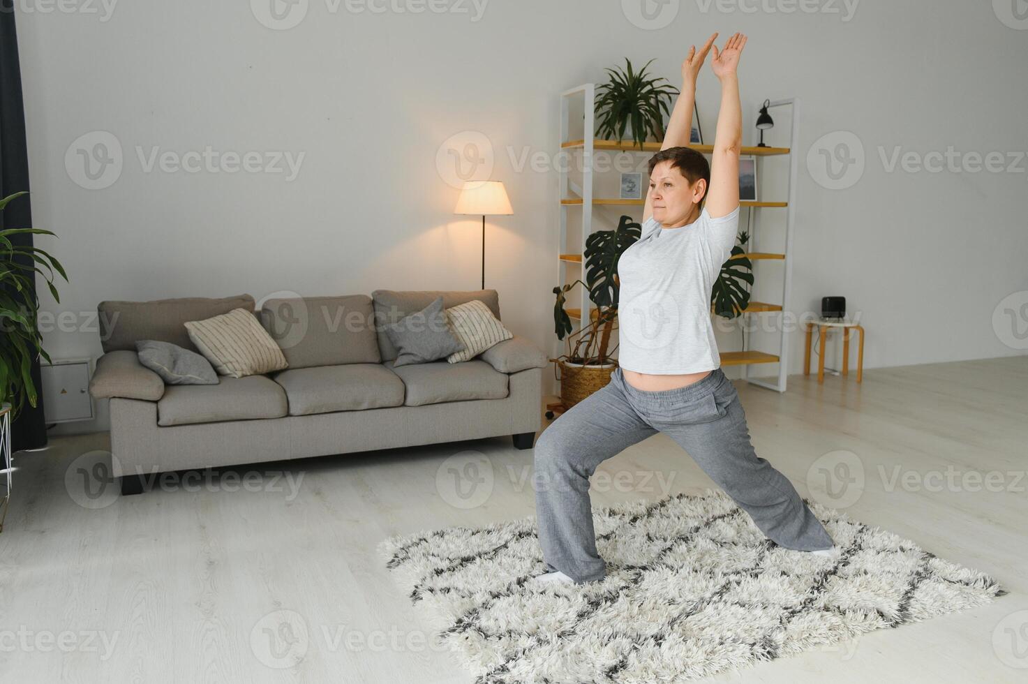 Working with your body. Full length of beautiful middle aged woman in sportswear doing pose lotus while sitinding in front of window at home. photo