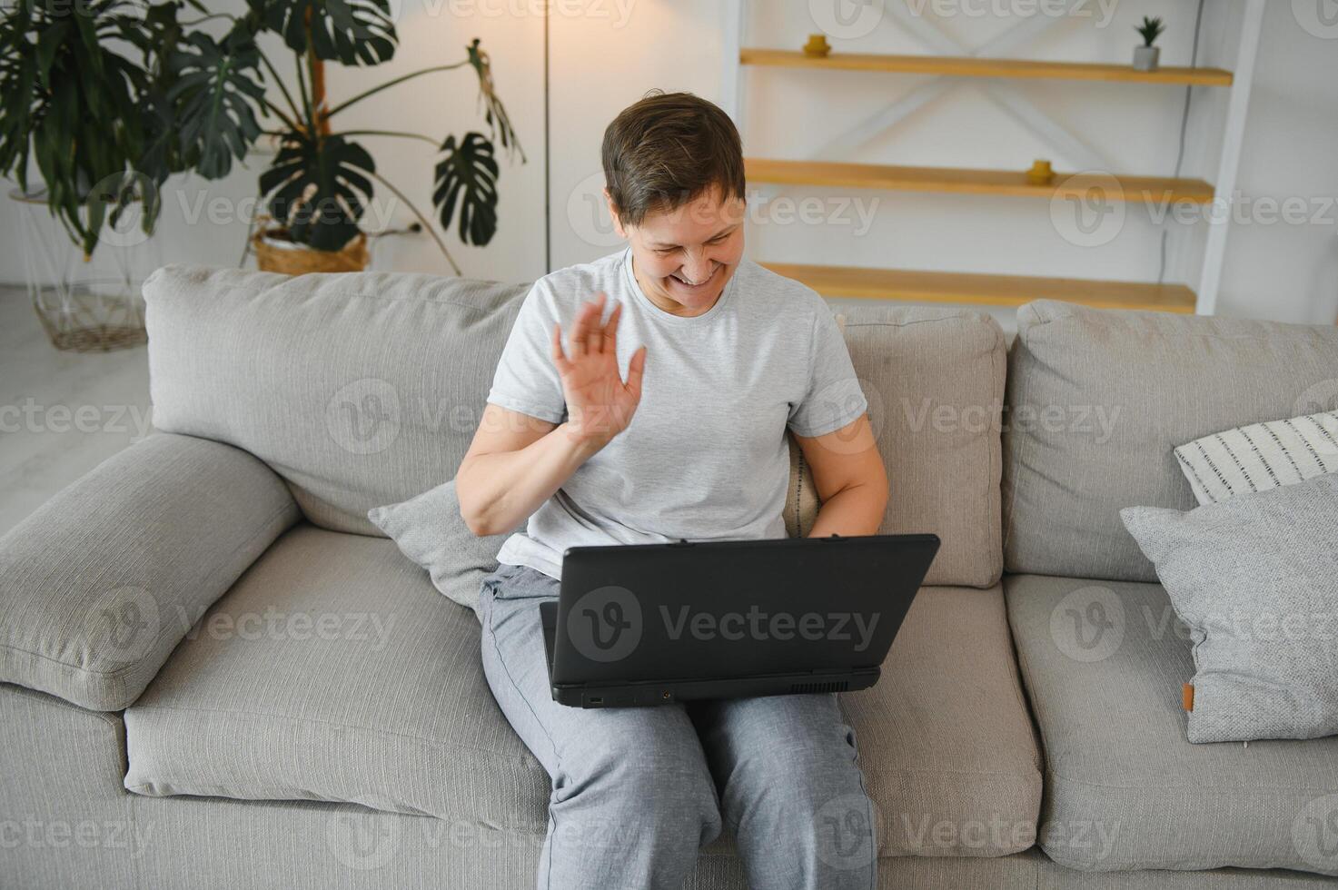 Older mature woman using wireless laptop apps browsing internet sit on sofa, smiling middle aged grandmother working distantly on computer surfing web communicating online looking at screen at home. photo