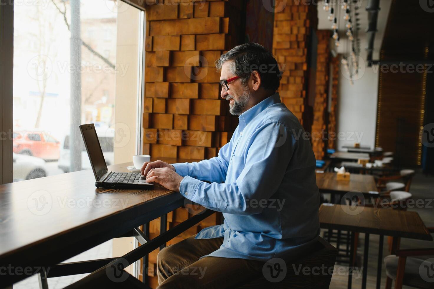 Male freelancer is working in a cafe on a new business project. Sits at a large window at the table. Looks at a laptop screen with a cup of coffee photo
