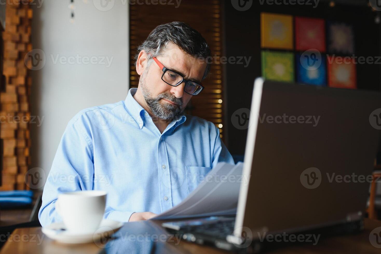 Male freelancer is working in a cafe on a new business project. Sits at a large window at the table. Looks at a laptop screen with a cup of coffee photo