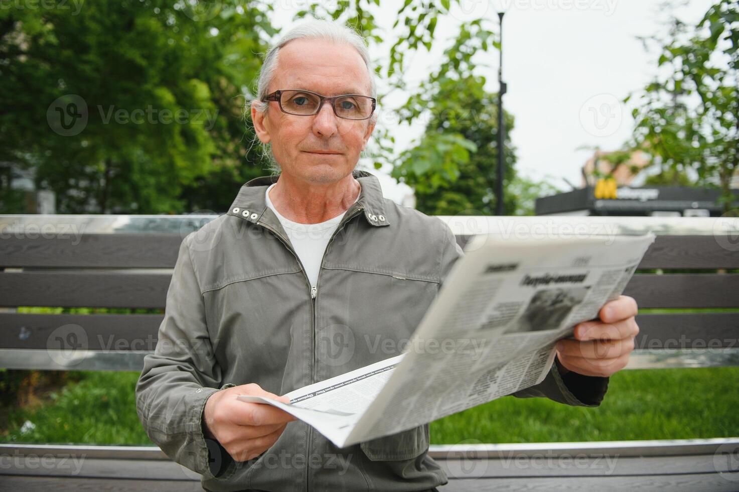 Portrait of senior man reading on bench during summer day. photo