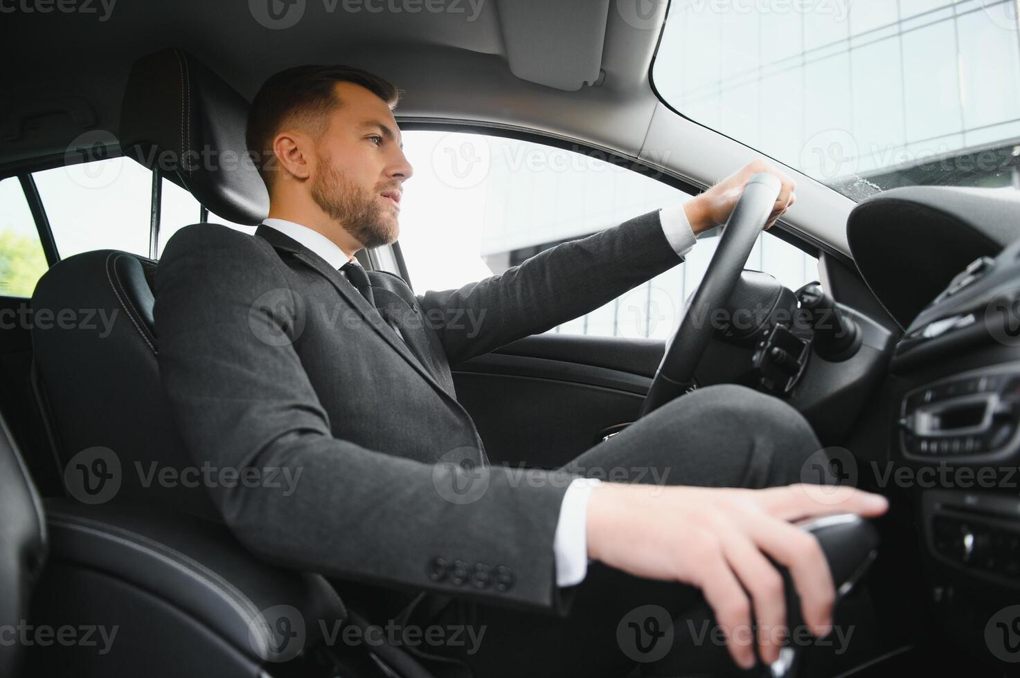Man of style and status. Handsome young man in full suit smiling while driving a car photo