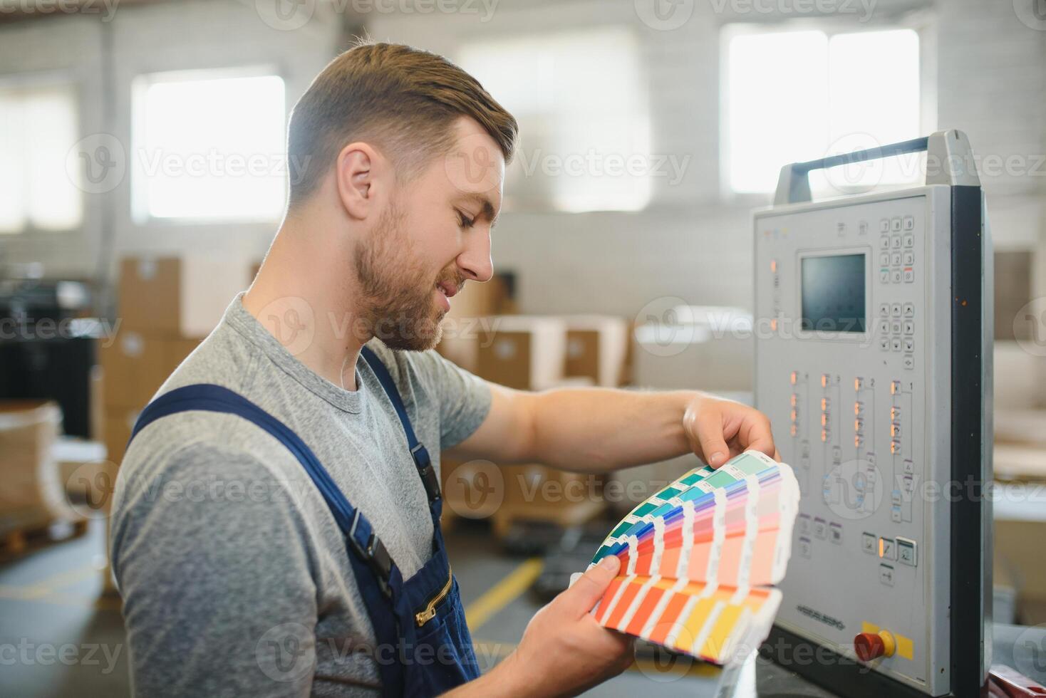 Portrait of production line worker controlling manufacturing process of modern packaging industrial machine in printing factory photo