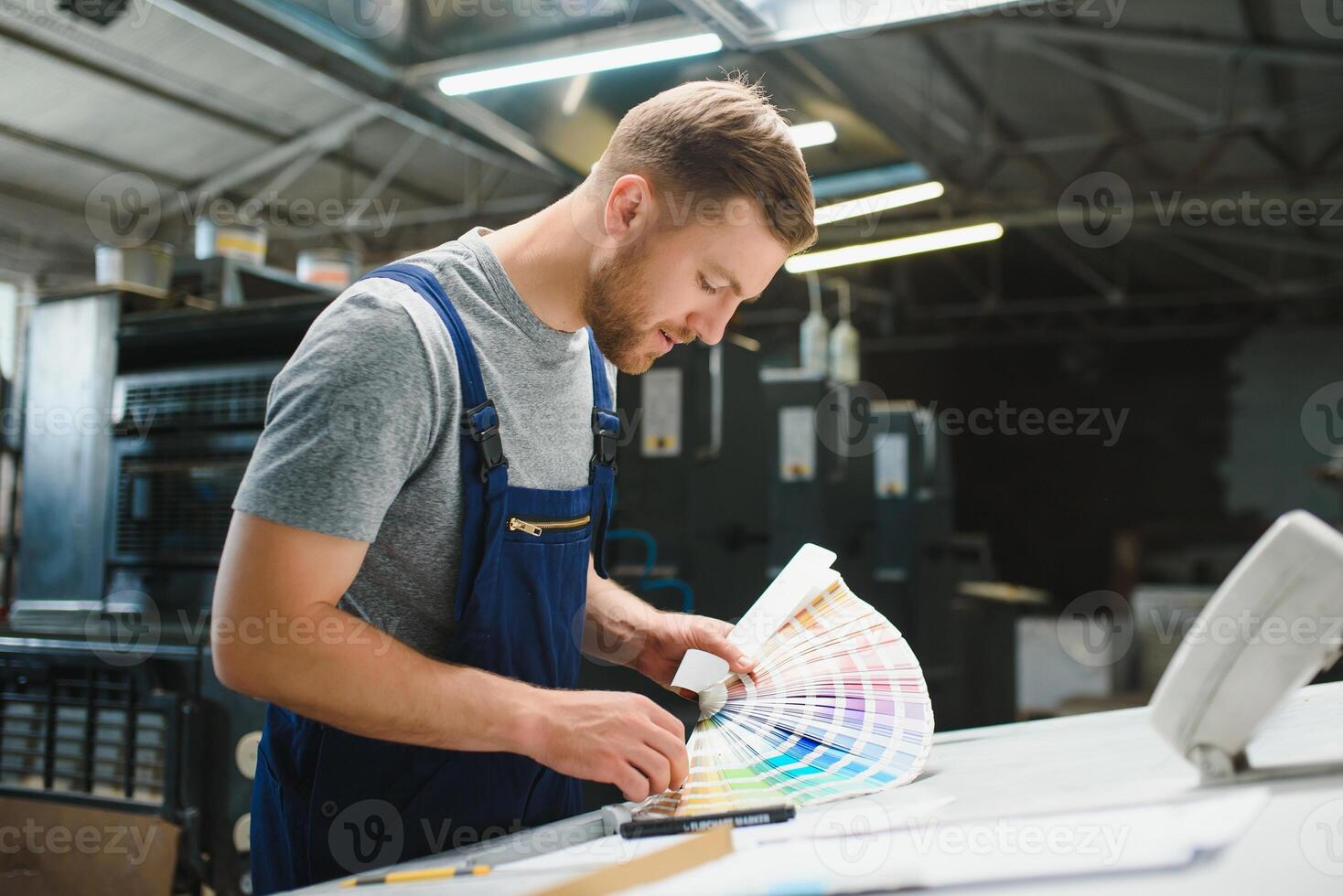 Portrait of production line worker controlling manufacturing process of modern packaging industrial machine in printing factory photo