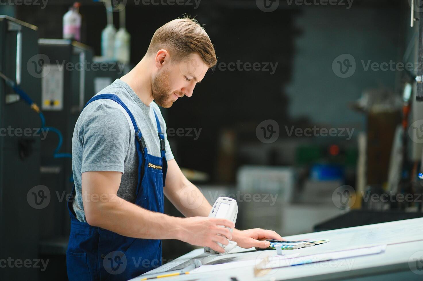Man worker measuring printing color with spectrometer on the operating desk of the printing plant photo