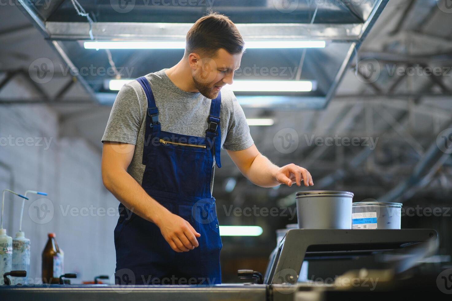 Portrait of production line worker controlling manufacturing process of modern packaging industrial machine in printing factory photo