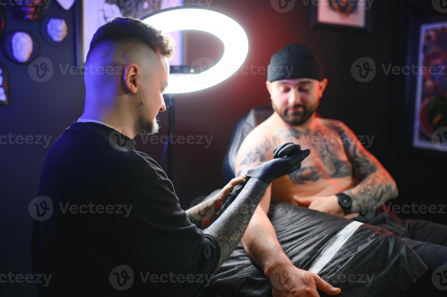 Male tattoo artist holding a tattoo gun, showing a process of making tattoos on a male tattooed model's arm photo