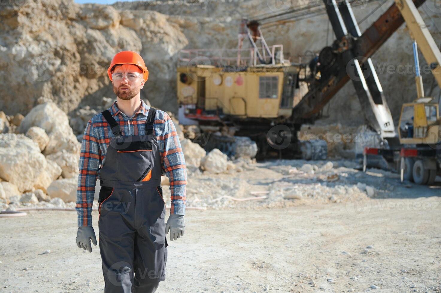 A worker in a helmet stands on the background of an excavator in a quarry photo