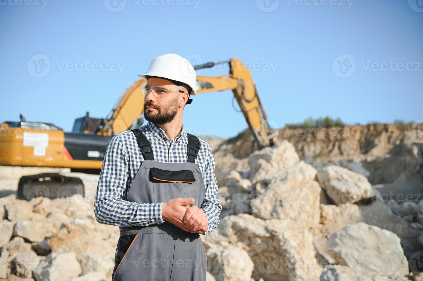 A worker in a helmet stands on the background of an excavator in a quarry photo