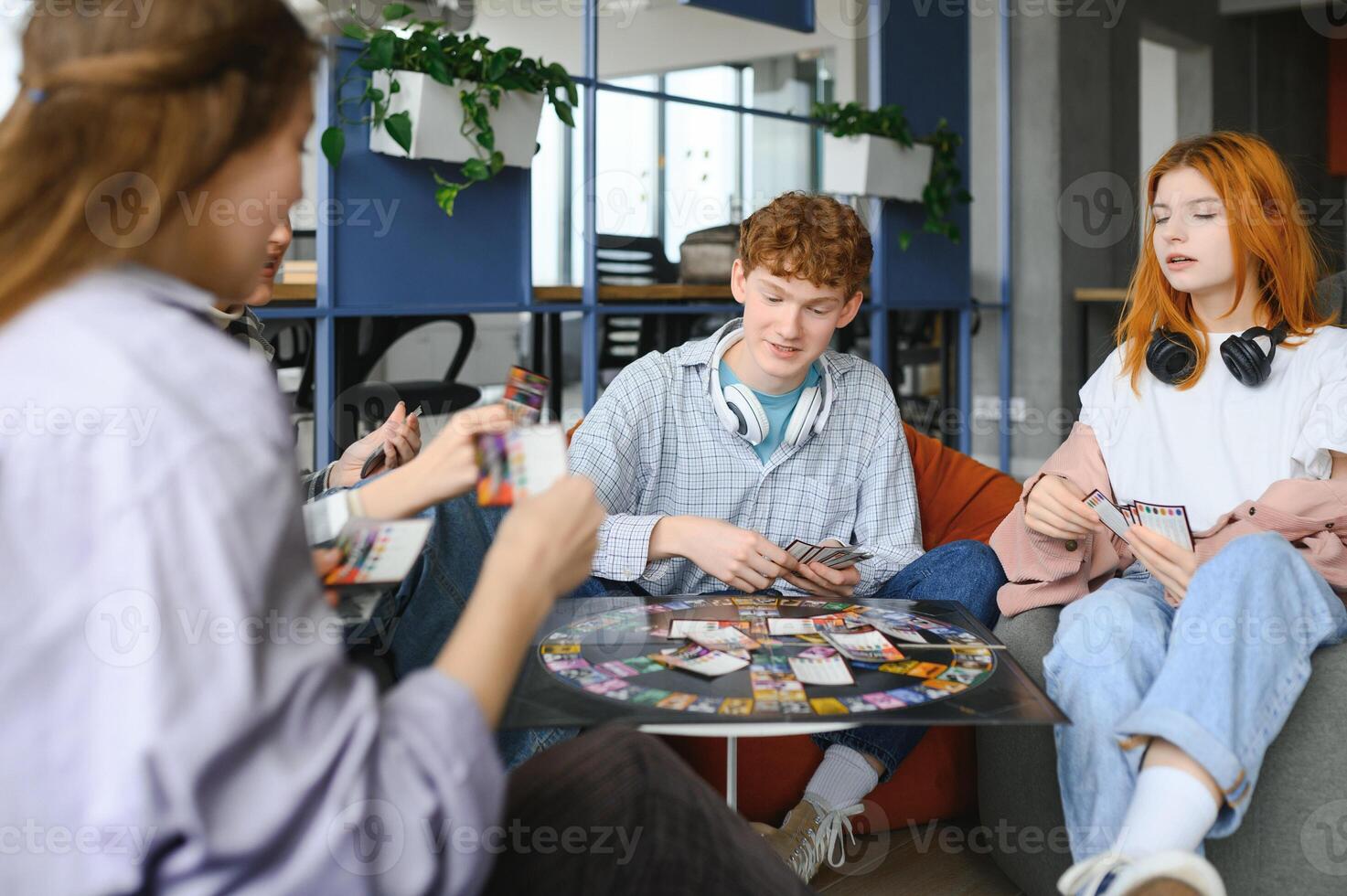 group of young friends playing board games together while sitting around table photo