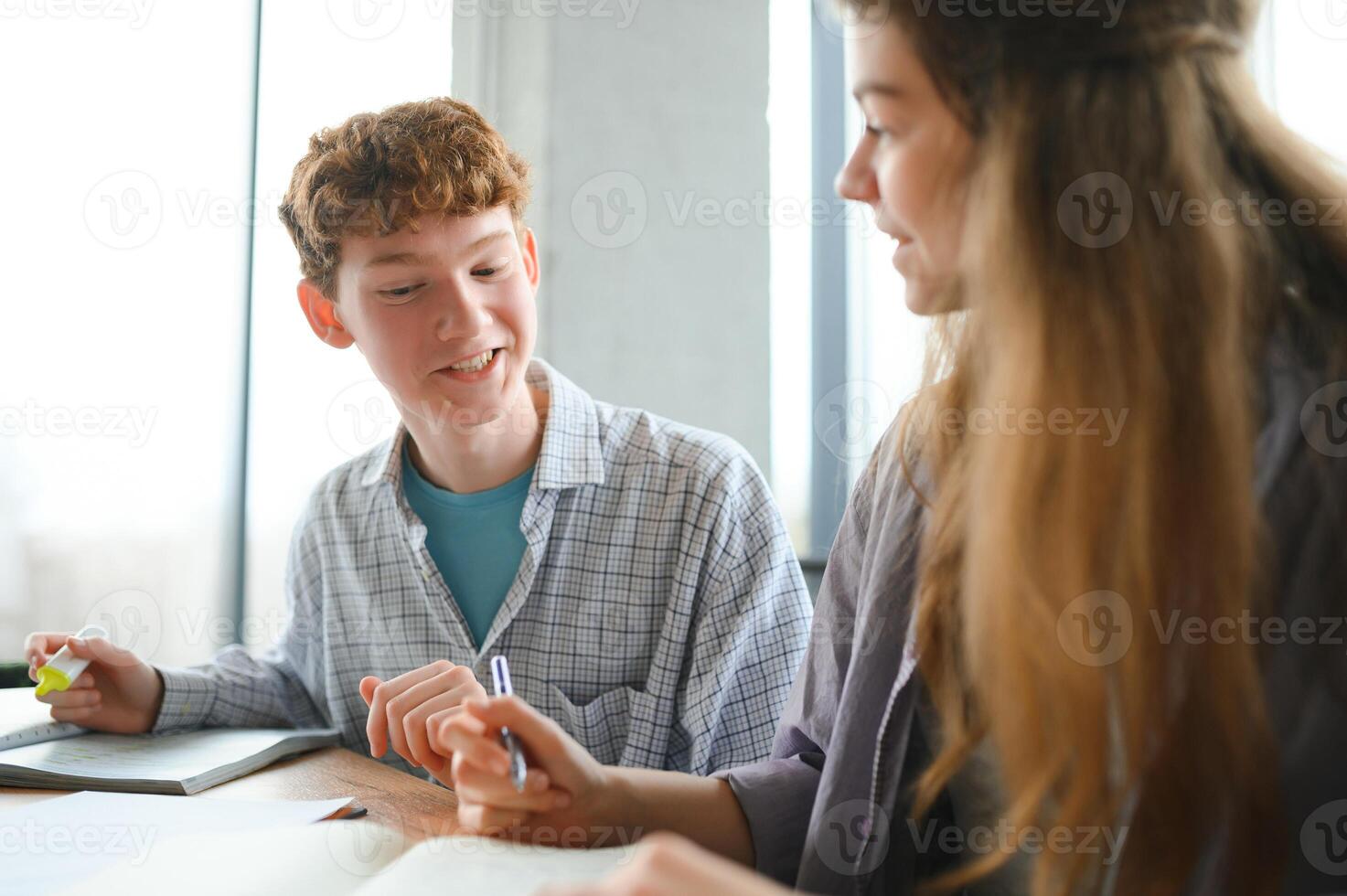 students sit at shared desk making notes studying together at university photo