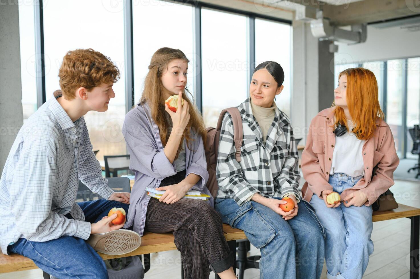 Cheerful students are sitting at desks and eating an apple during a break photo