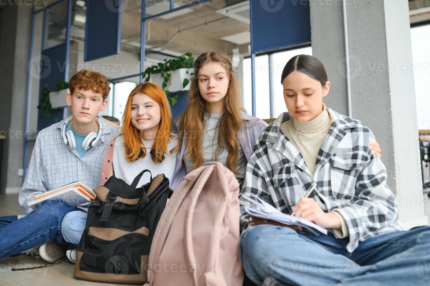 A group of cheerful student friends are sitting on the floor in a classroom photo