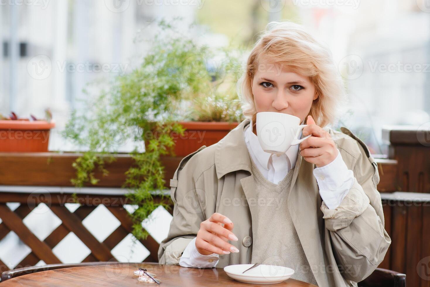 Fashion portrait of young woman siting at the table with cup of coffee, tea in street cafe. photo