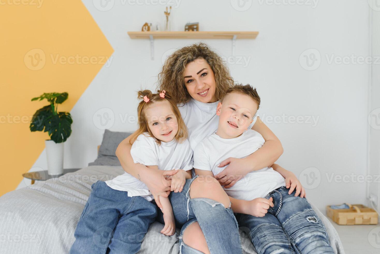 Portrait of smiling young mommy embracing kids little son and daughter. Happy family. Mother with children sitting on bed and loving the good times together. Closeup photo