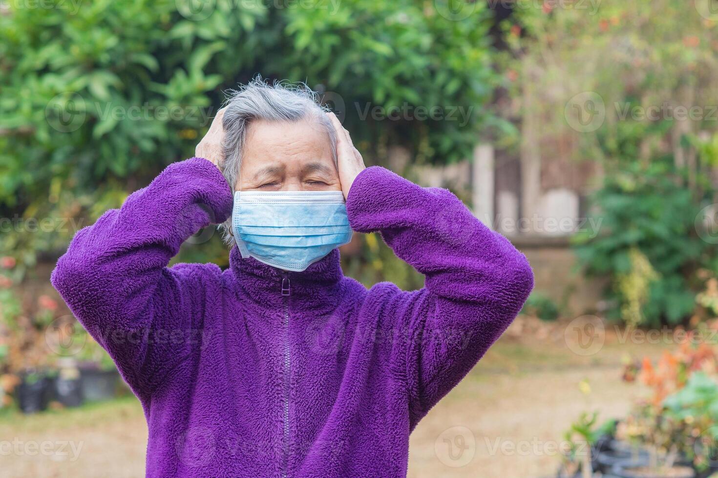 A senior woman wearing a face mask has a headache while standing in a garden. Mask for protection Covid-19, virus, bacteria, etc. Concept of aged people and healthcare photo