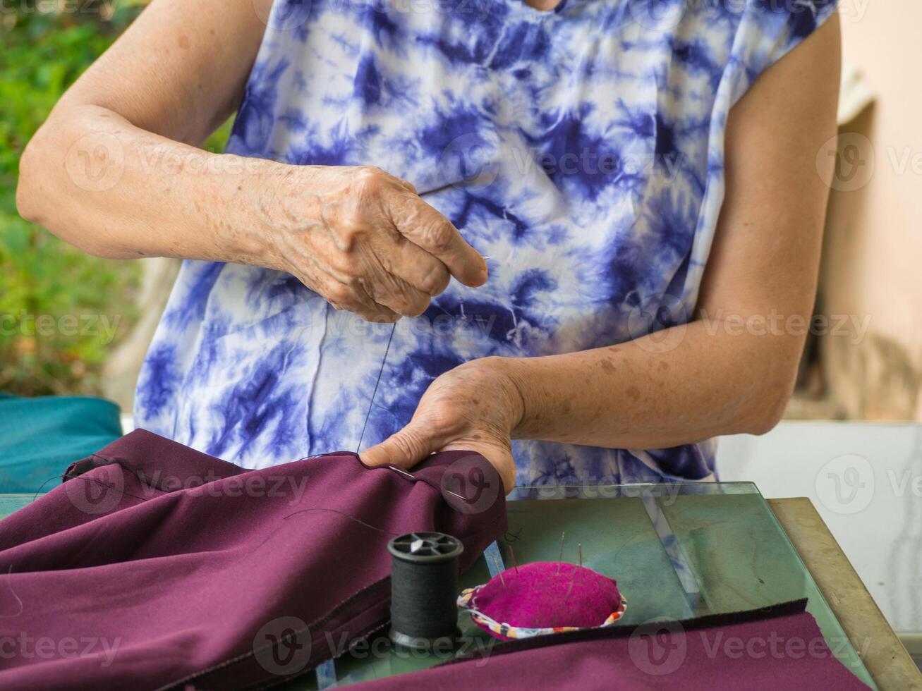 Close-up of hands senior woman's trying to thread a needle for sewing cloth. Space for text. Concept of aged people and relaxation photo