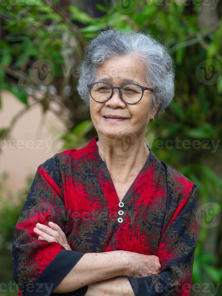 Portrait of a beautiful senior woman smiling with arms crossed while standing in the garden photo
