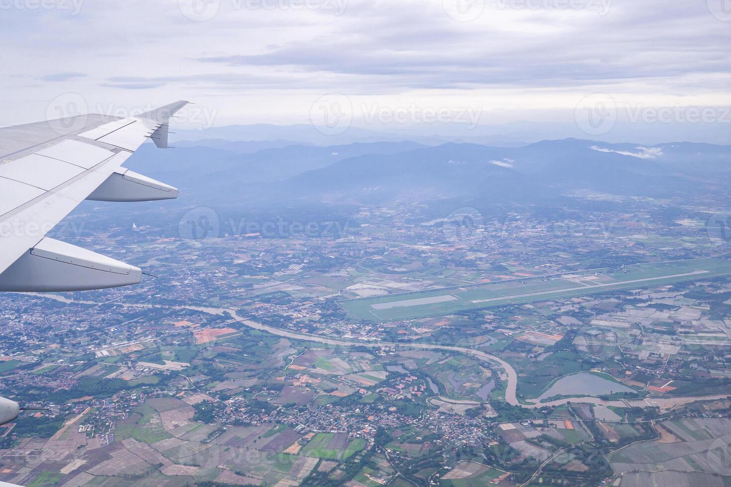 Aerial view of agricultural field, river, mountains, and clouds are seen through the airplane window photo