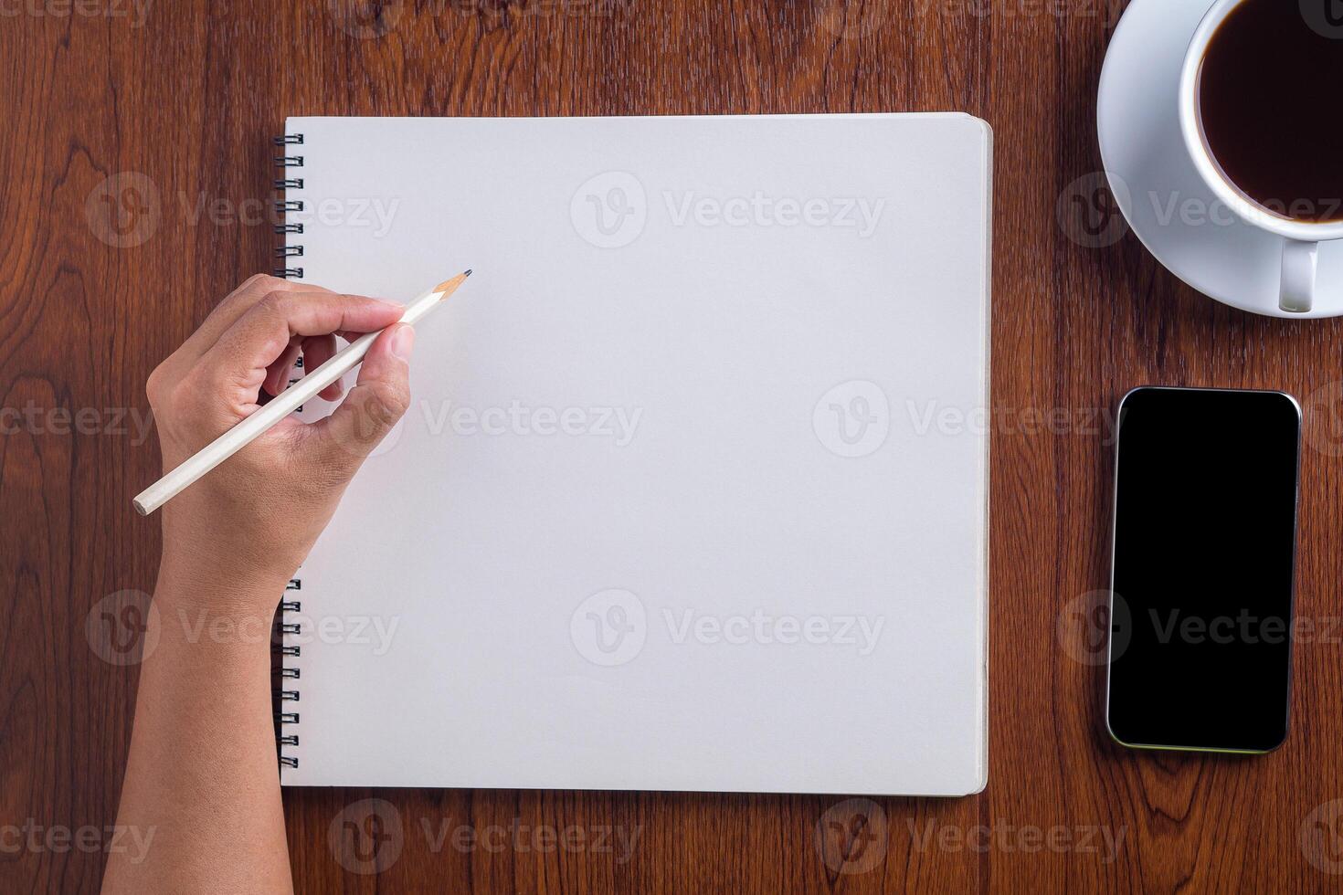 Close-up of hand woman holding a pencil prepare for drawing on sketchbook placed on wooden table. Wood texture background. Concept of drawing and technology photo