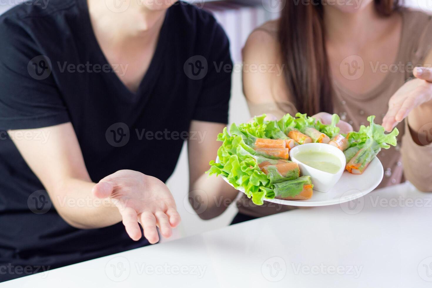 Close-up of a young couple holding a dish of fresh vegetables while sitting on a chair in the kitchen. Foods for diet, low calories. Eat vegetables organic for good health. Health foods concept photo