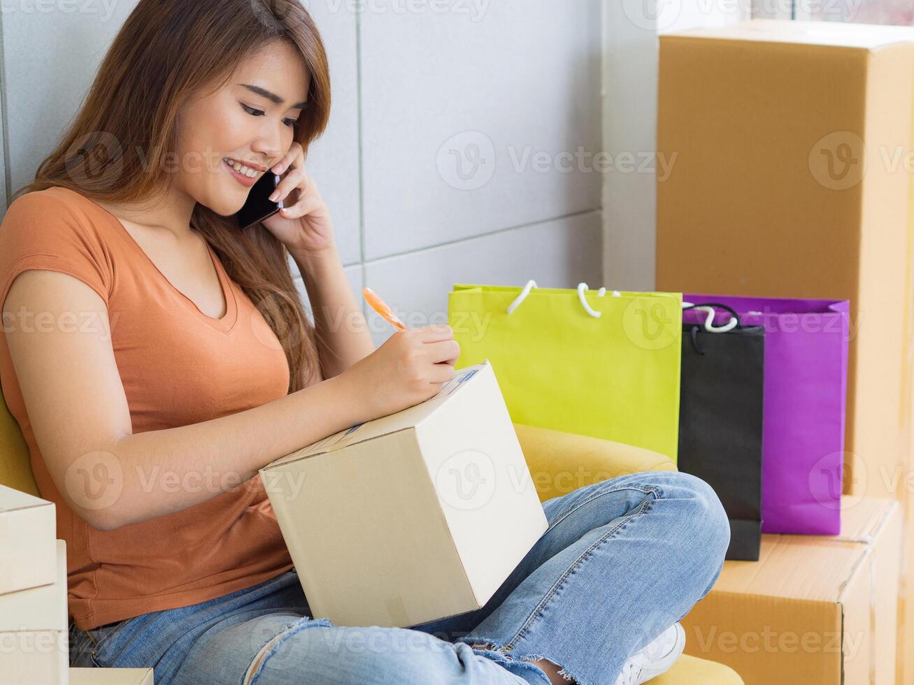 Businesswoman using a smartphone, smiling and write data on cover parcel box for prepare send to customer. Concept of business and e-commerce photo