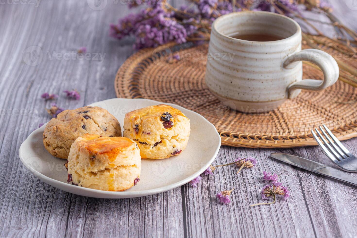 Close-up of traditional British scones dessert and a cookie on a plate with a teacup and flower blurred background. Space for text. Concept of dessert and tea photo