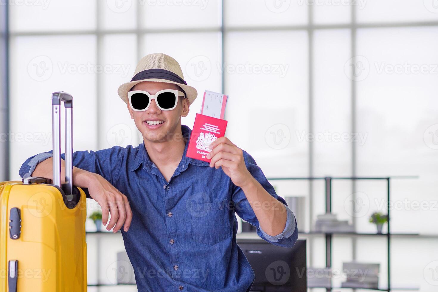 Young man wearing a blue shirt, sunglasses, and hat, smiling and showing a plane ticket. Space for text. Concept of holiday and travel photo