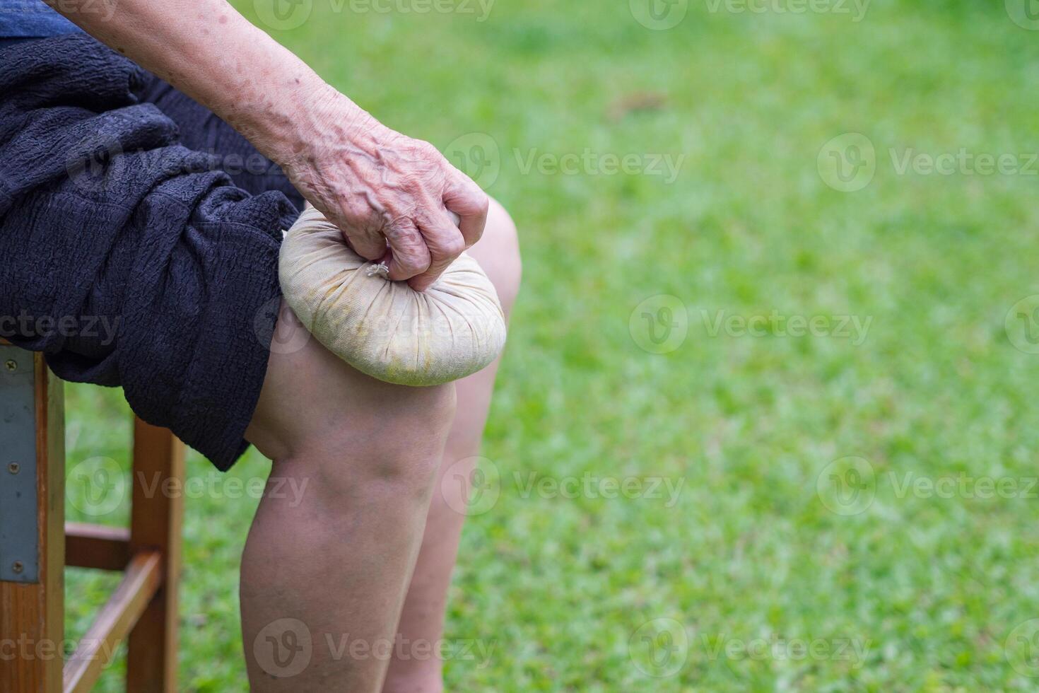 A senior woman uses a Thai herbal compress ball on the knee. Knee pain may cause by muscle strain, tendinosis, osteoarthritis. photo