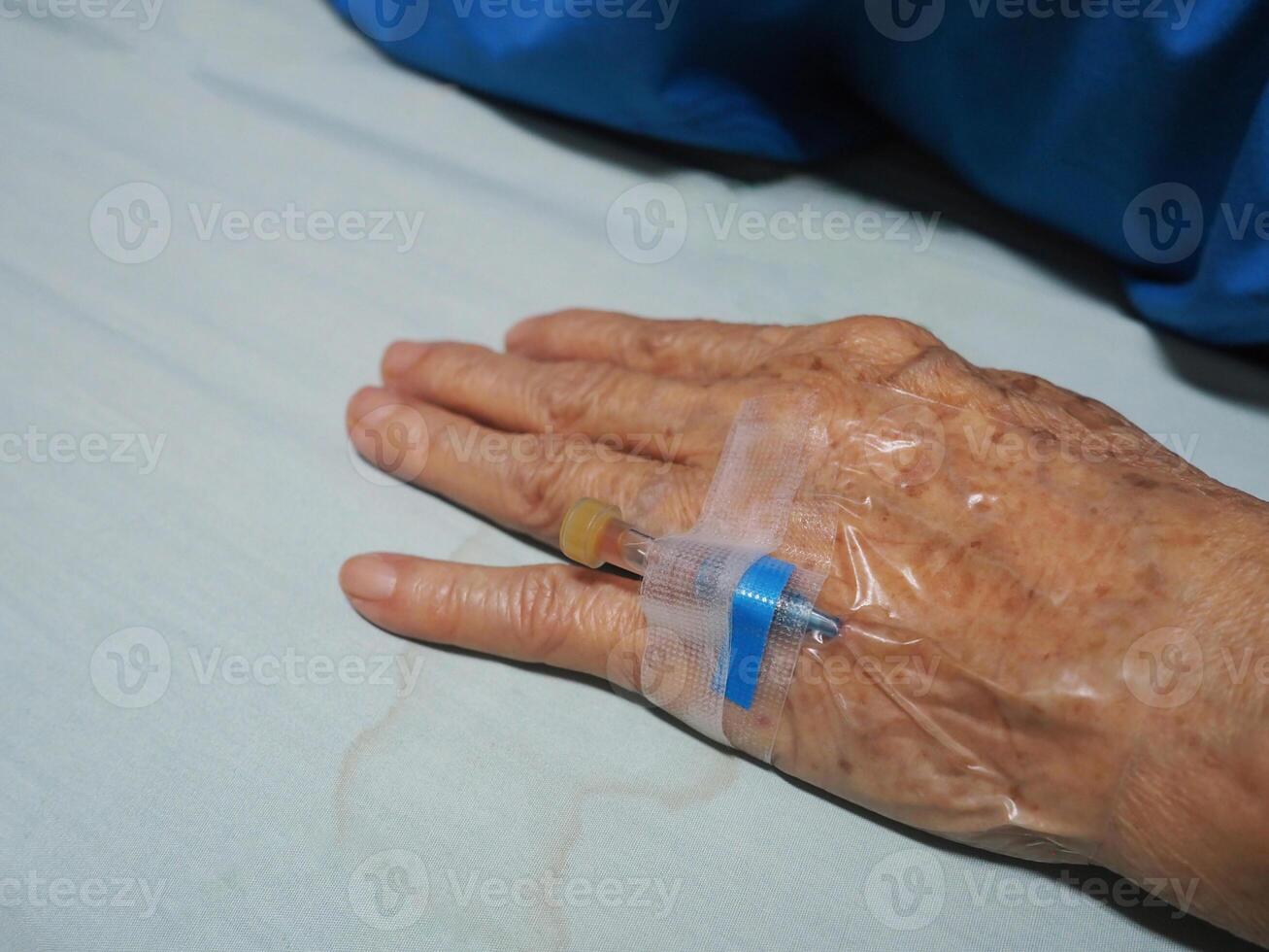 Close-up of a syringe implanted on the hand of a senior woman patient admitted to the hospital. Concept of aged people and healthcare photo