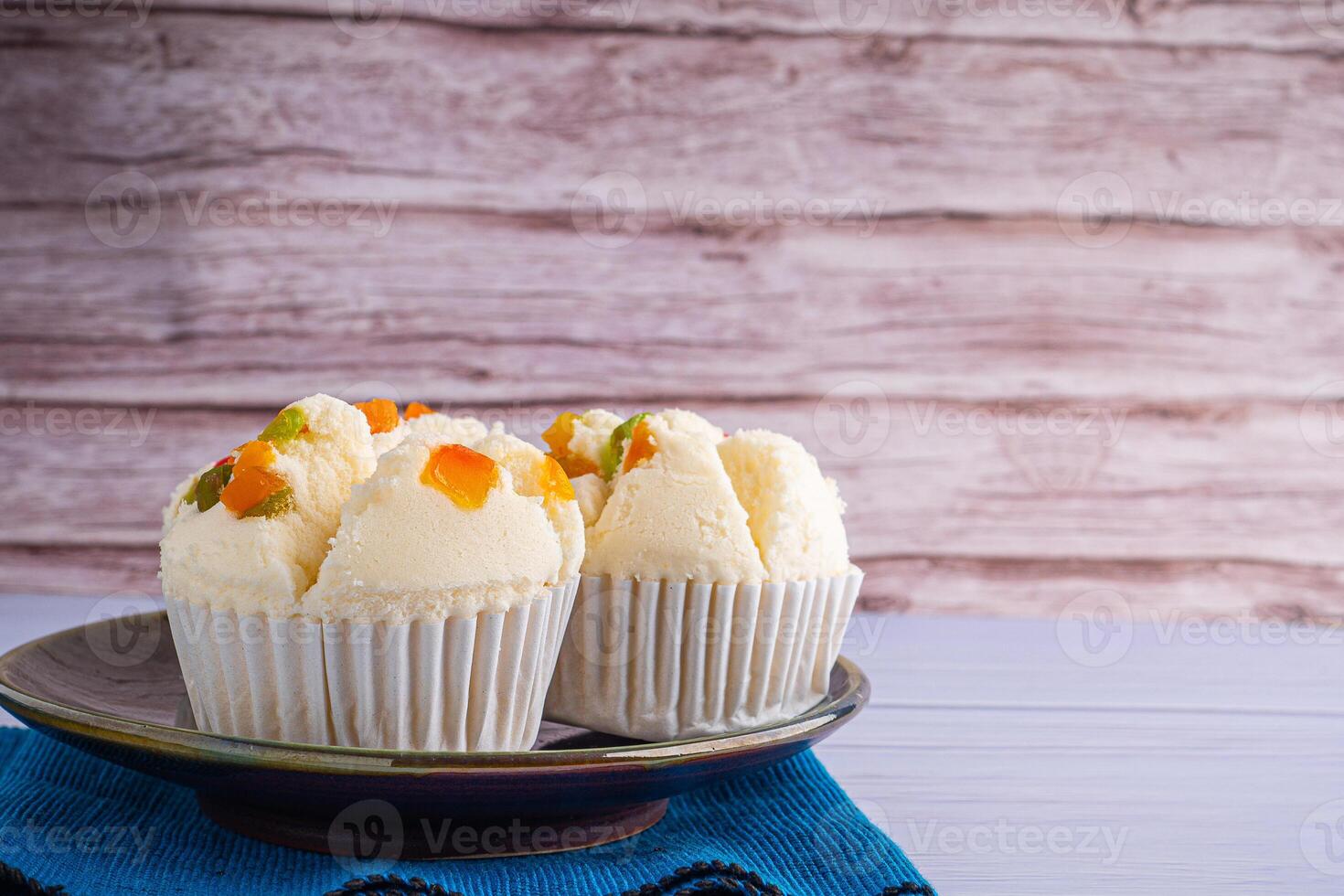Side view of Thai steamed cupcakes topped with dry fruit on a plate placed on a blue cloth with wooden wall background. Khanom Pui Fai in Thai photo
