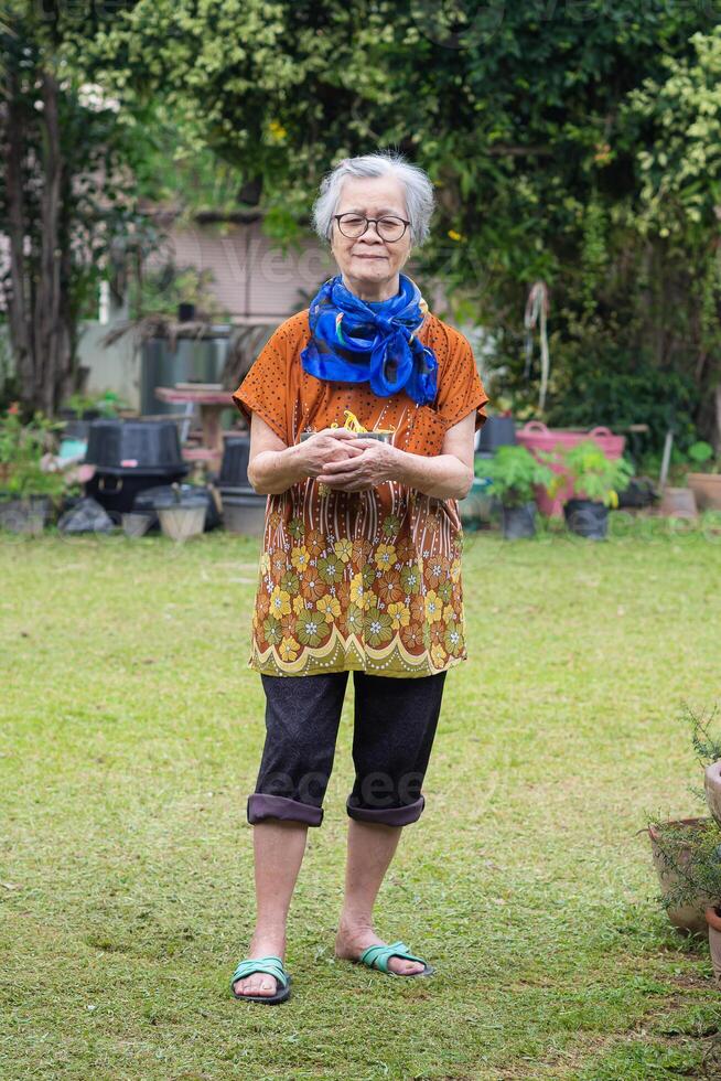 Portrait of an elderly woman looking at the camera while standing in a garden photo