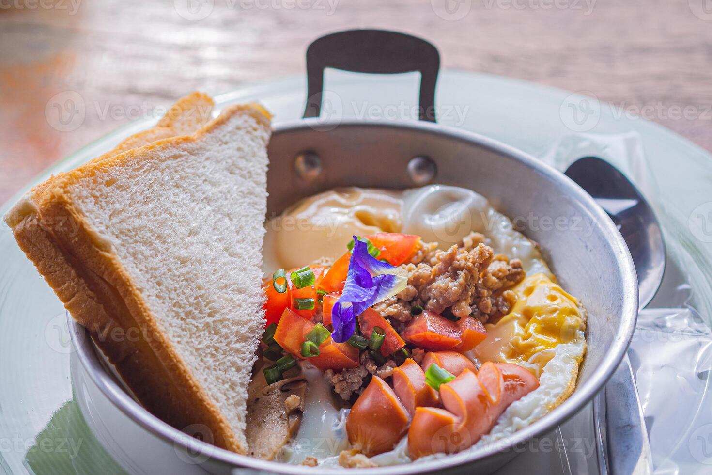 Close-up of fried eggs with bacon, hotdog, fresh tomato, and bread on a pan. Breakfast set photo