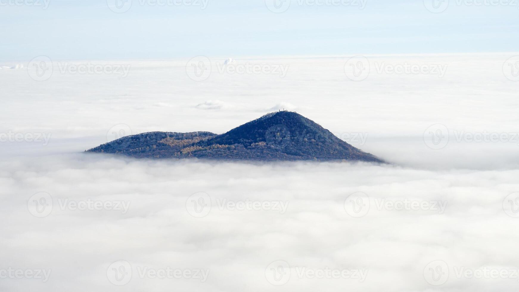 A lone mountain peak emerges above a dense sea of clouds under a clear sky photo