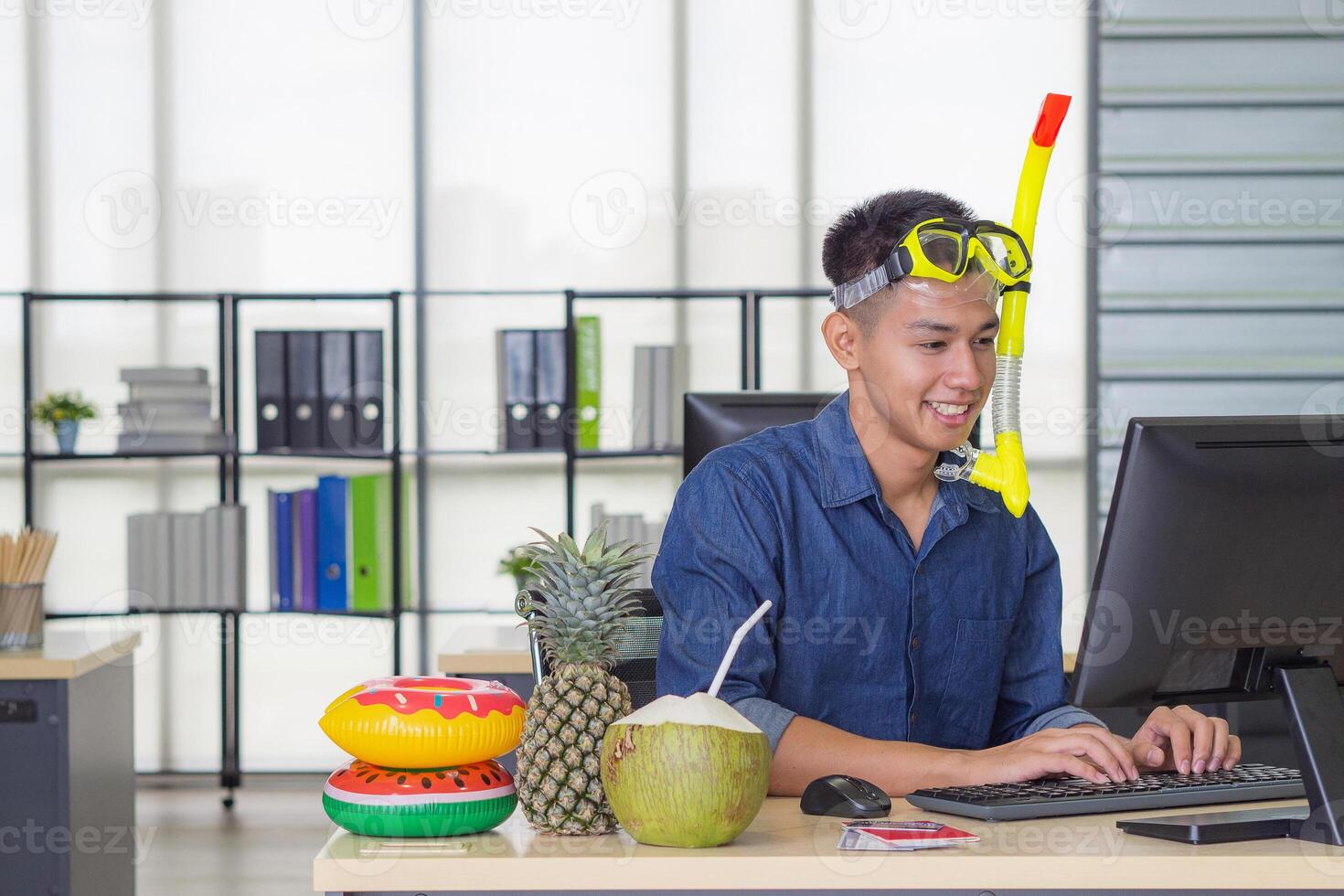 Young man wearing a diving mask yellow and sitting on a chair working in the office. He dreams of the sea because the holiday coming soon. Holiday concept photo