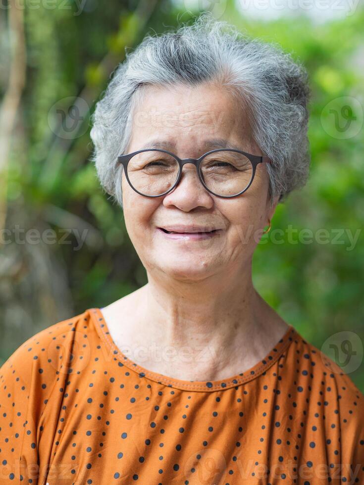 Portrait of a senior woman with short gray hair wearing glasses, smiling and looking at the camera. Space for text. Concept of aged people and relaxation photo